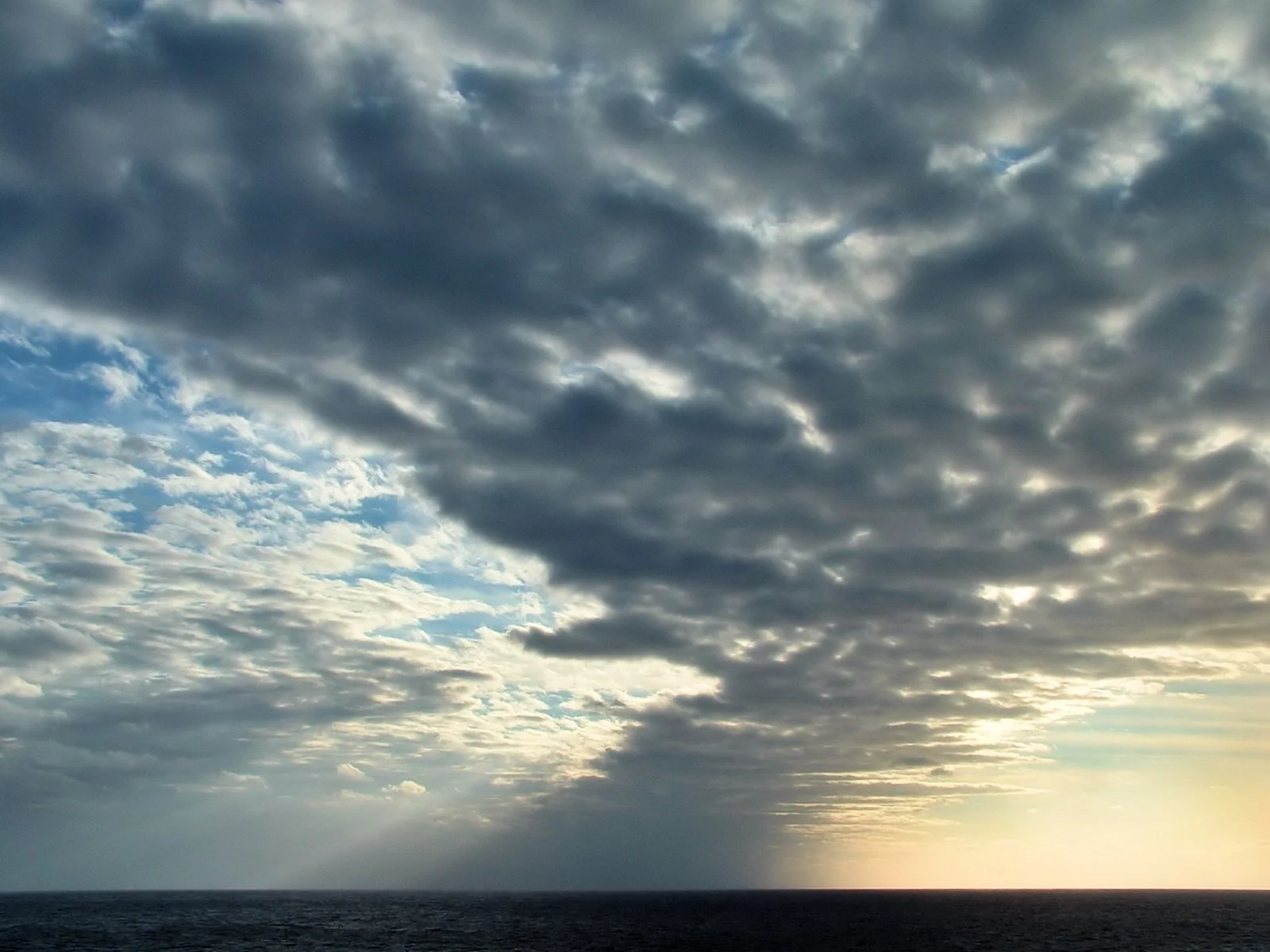 空の半分を覆う灰色の雲と、右下の水平線近くに明るく差す朝の光。手前は暗い海。