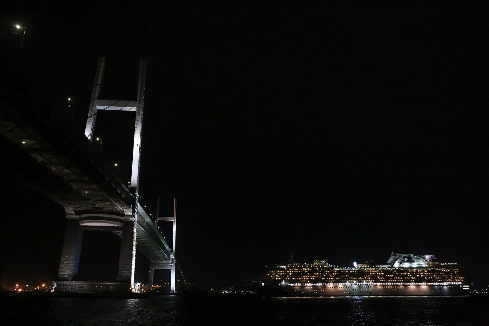 夜、明かりのともった斜張橋の下の海に、窓の明かりが並ぶ大型客船が浮かぶ。
