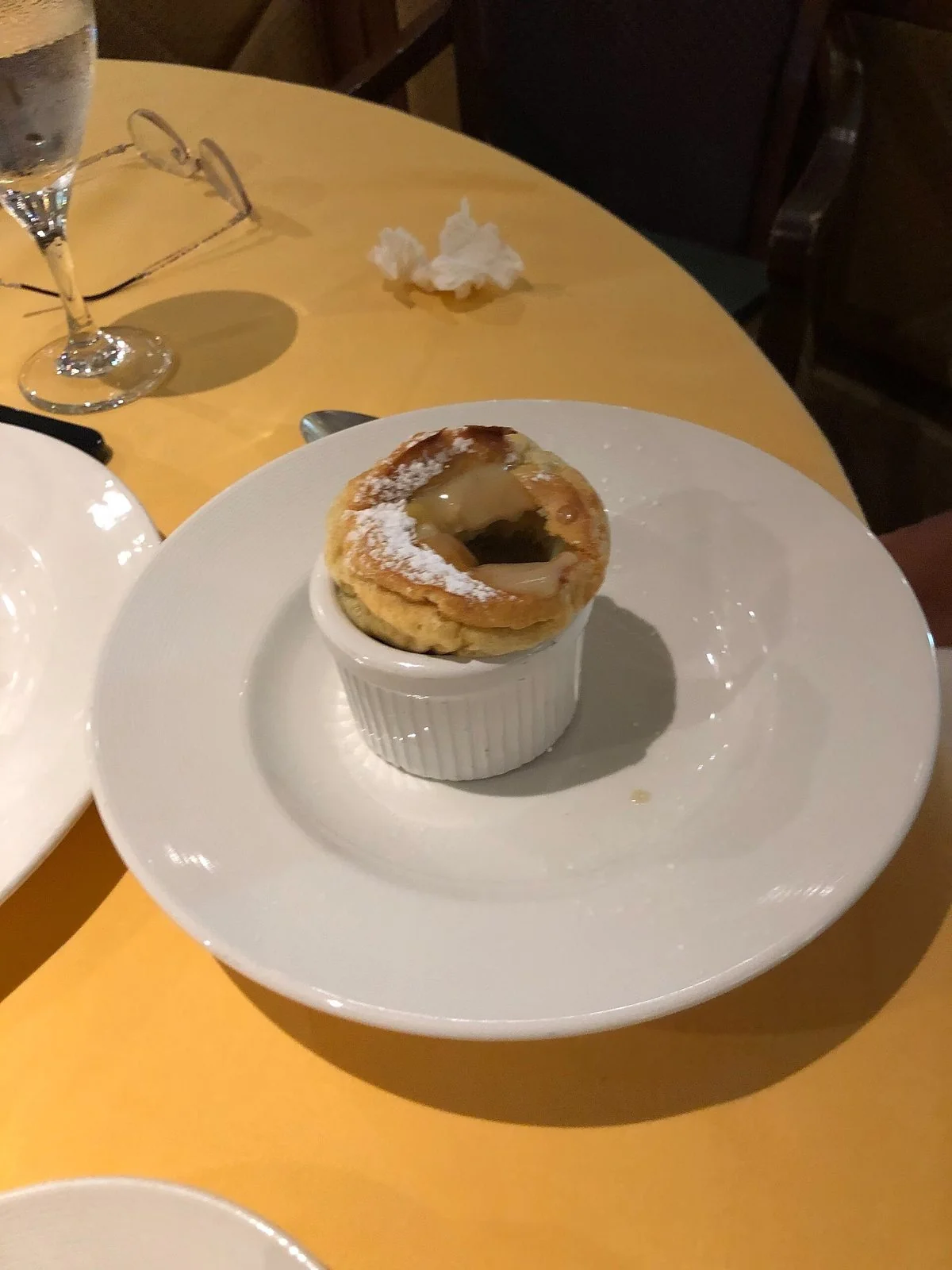 黄色いテーブルクロスの上の白い皿に、粉砂糖をかけた焼き菓子の器が置かれている。奥にグラスと眼鏡。
