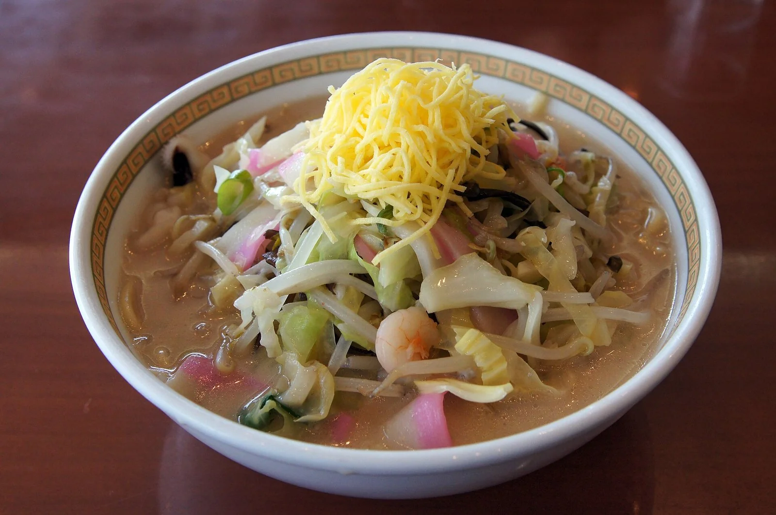 白い丼に、キャベツやもやし、ピンクのかまぼこ、えびがのったちゃんぽん。上に黄色い錦糸卵。