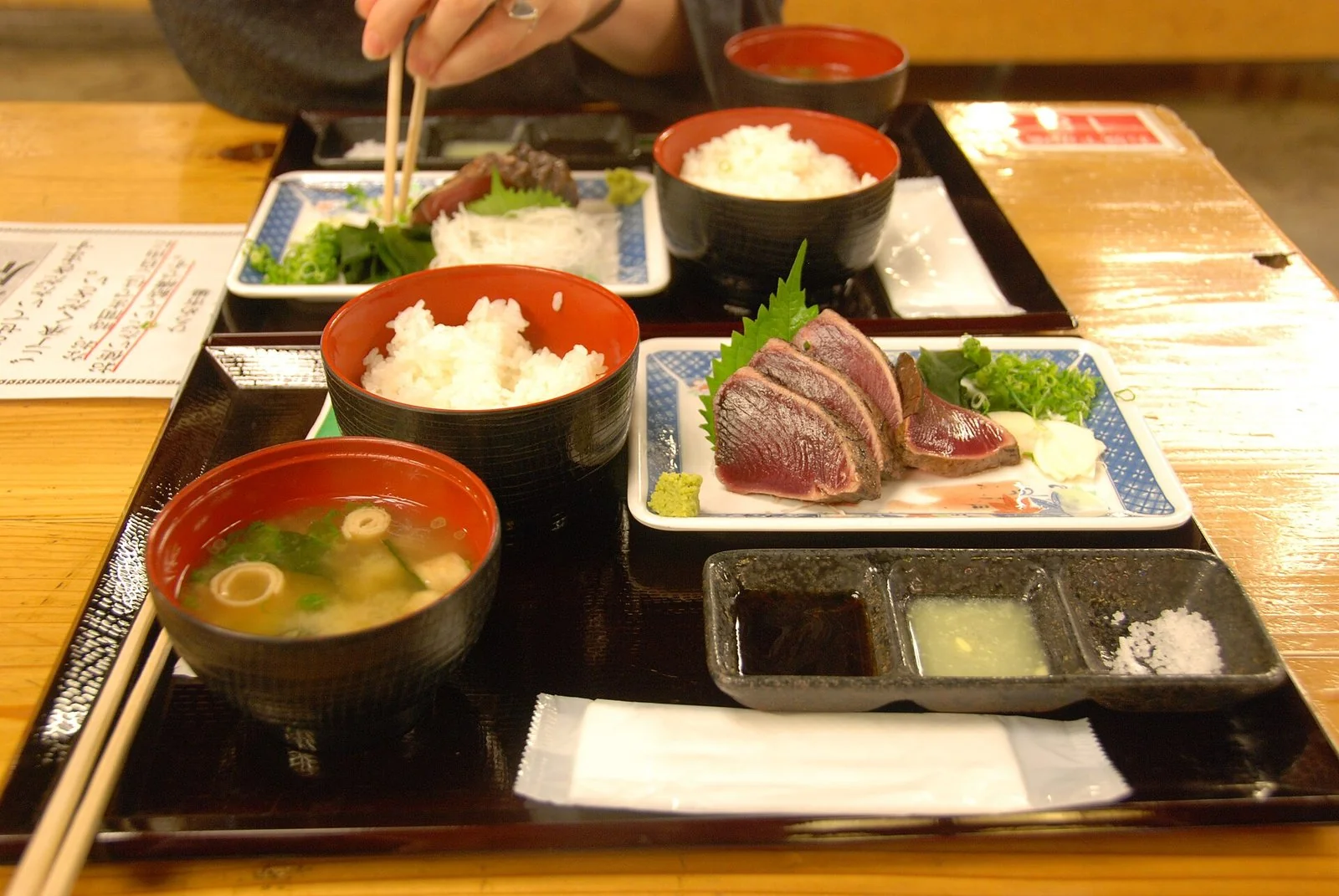 黒い盆に、かつおのたたきの皿とご飯、味噌汁、塩とたれの小皿が並ぶ定食。