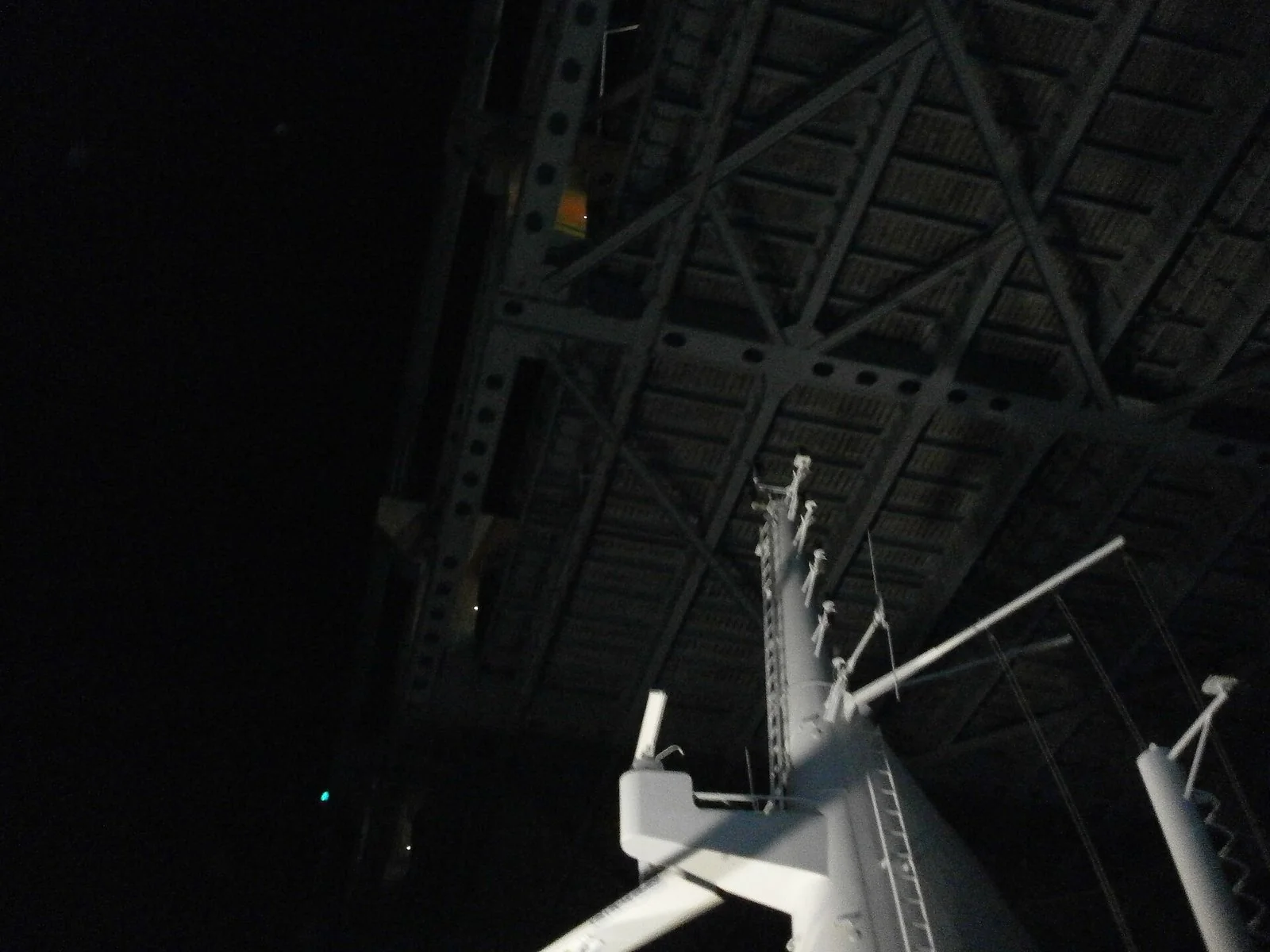 暗い空の下、白い船のマストのすぐ上に、橋の鉄骨の裏側が大きく迫っている。